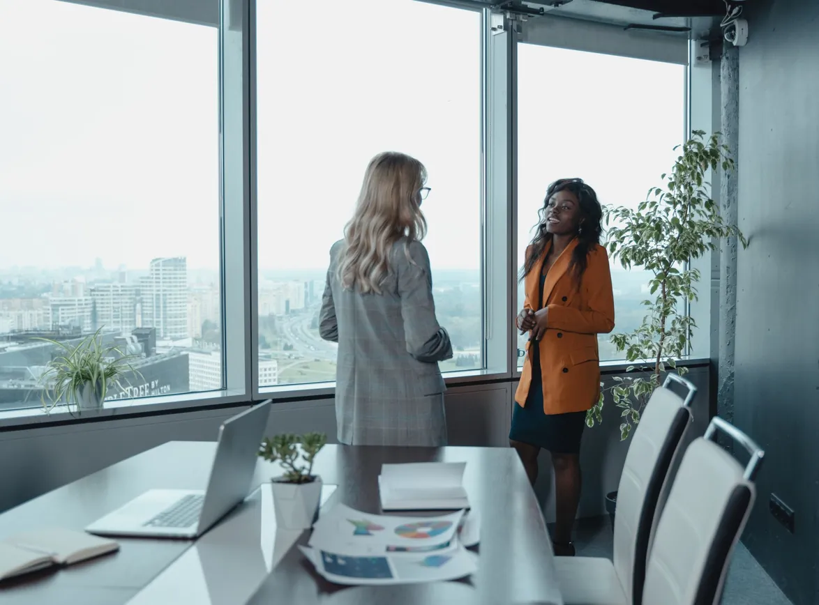 Two women engage in a business discussion in an office with city view