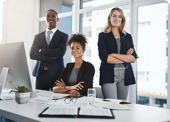 Three business professionals posing in an office, two standing with arms crossed and one seated at a desk