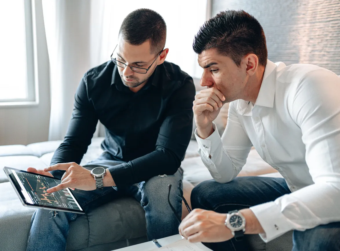 Two businessmen analyzing financial data on a tablet indoors