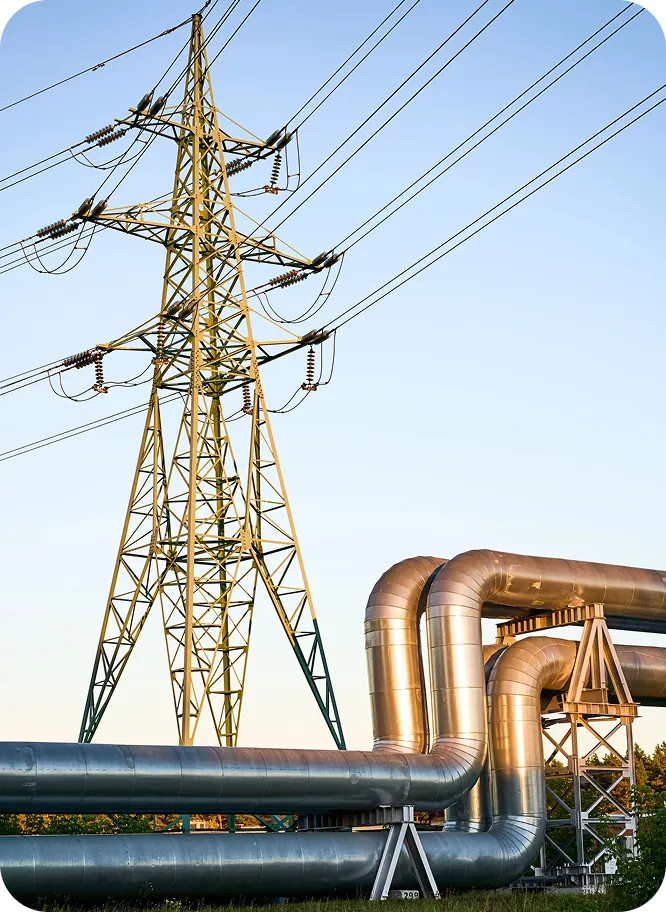 High-voltage transmission tower and power lines above insulated pipelines against a clear sky