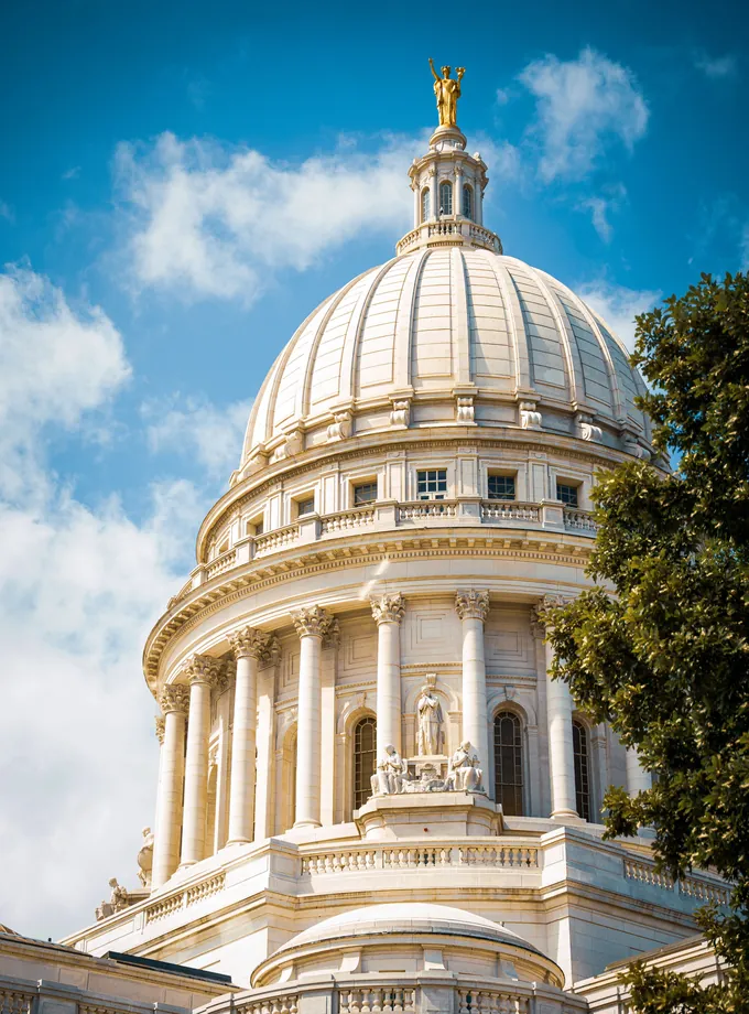 White marble dome of the Wisconsin State Capitol with a gold statue on top against a blue sky