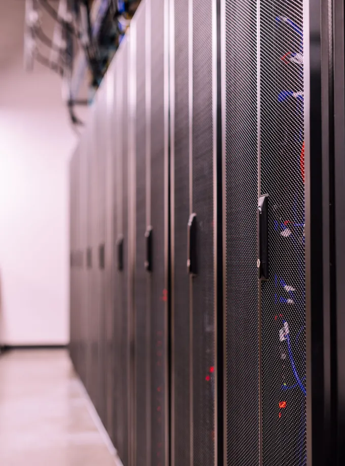 Row of black mesh-door server racks with blue cabling lining a data center aisle