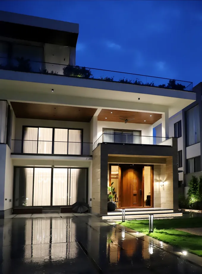Modern two-story house with glass balconies and a lit wooden front door at dusk