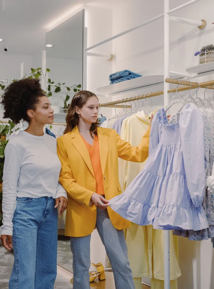 Two women browsing pastel dresses on a clothing rack in a bright, minimalist boutique