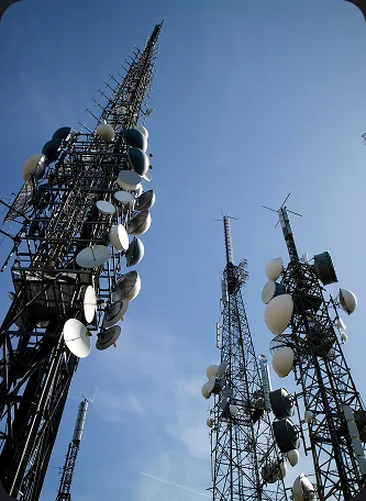 Telecommunications towers fitted with satellite dishes and antennas against a blue sky