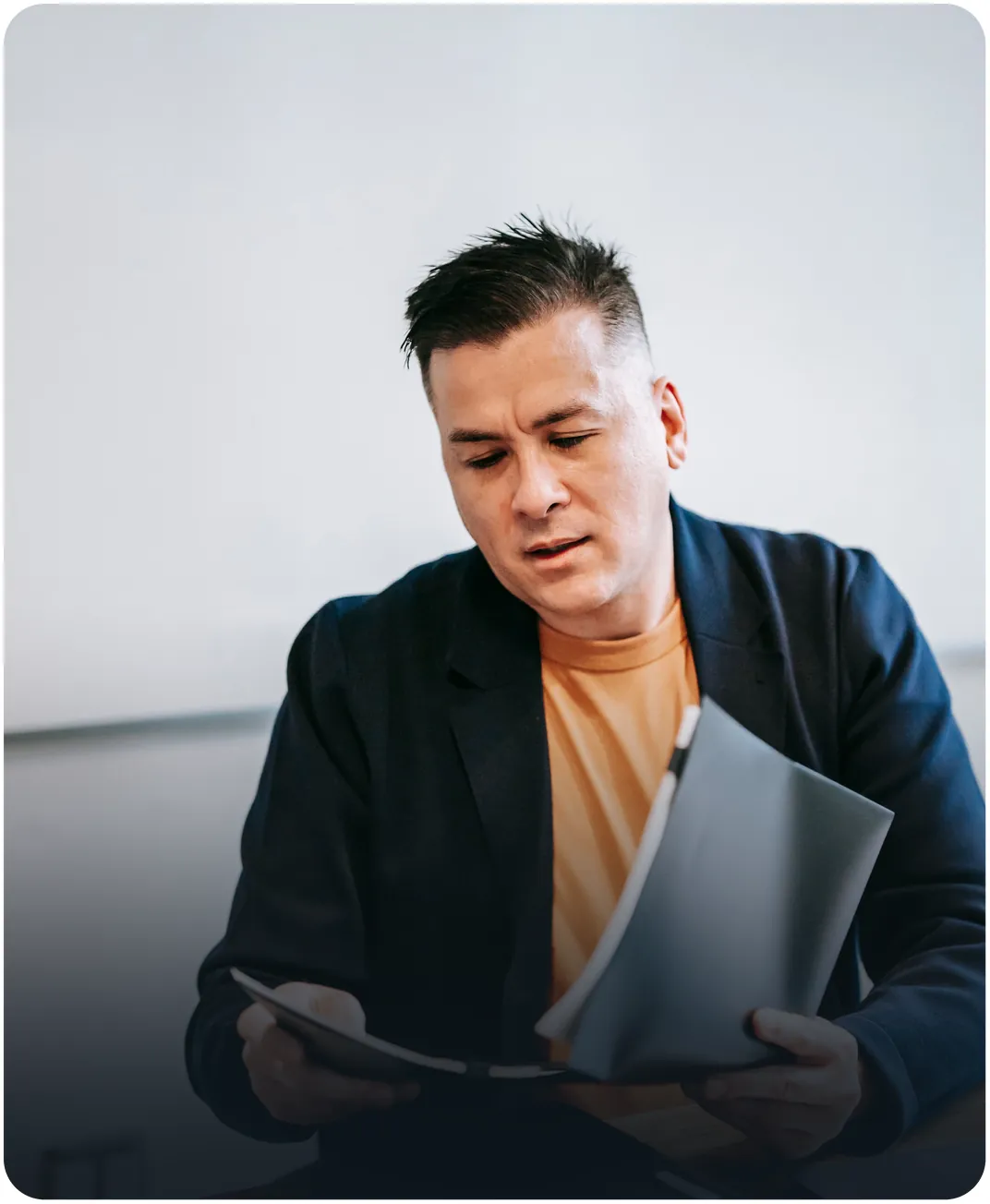 Businessman in a navy blazer reading through a printed report in a bright office