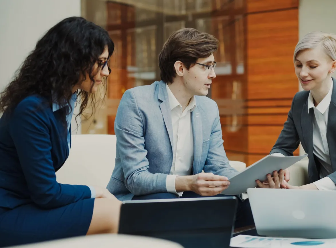 Three professionals discussing over a tablet in a modern office setting