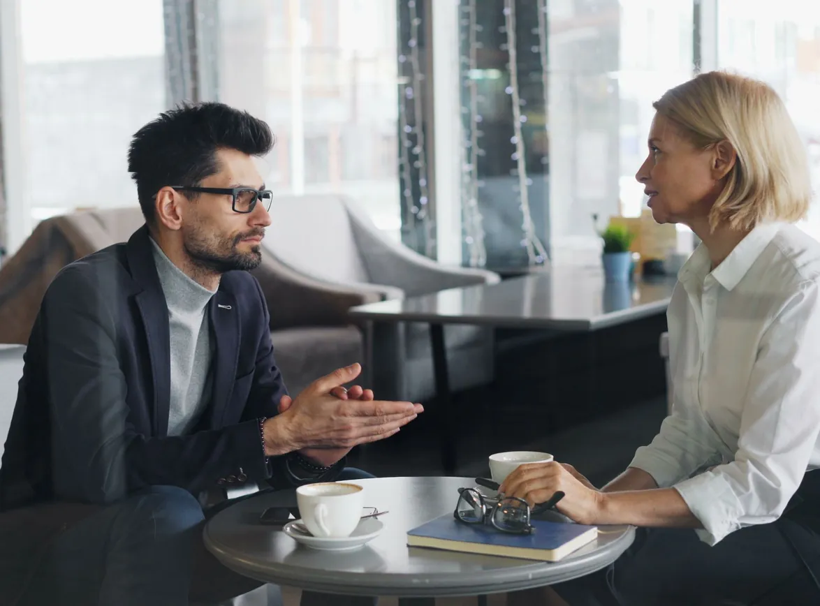Consultant in glasses talking with a client over coffee at a cafe table