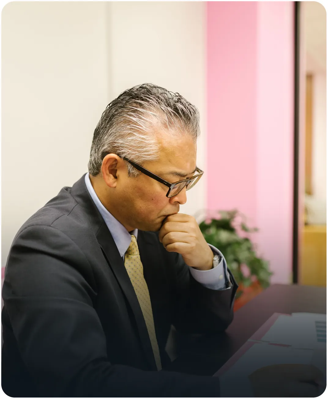 Businessman in a suit and glasses resting his chin on his hand while studying printed reports at his desk