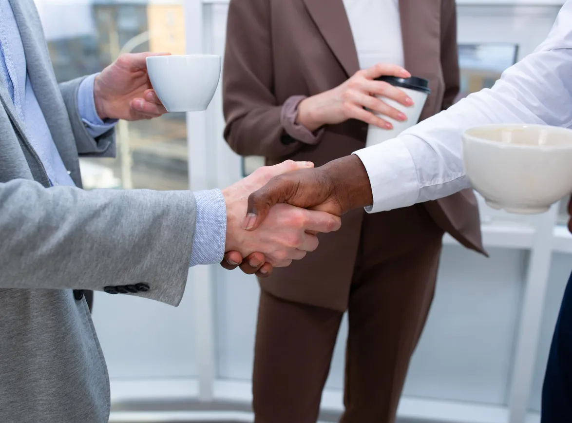 A professional handshake between colleagues holding coffee cups