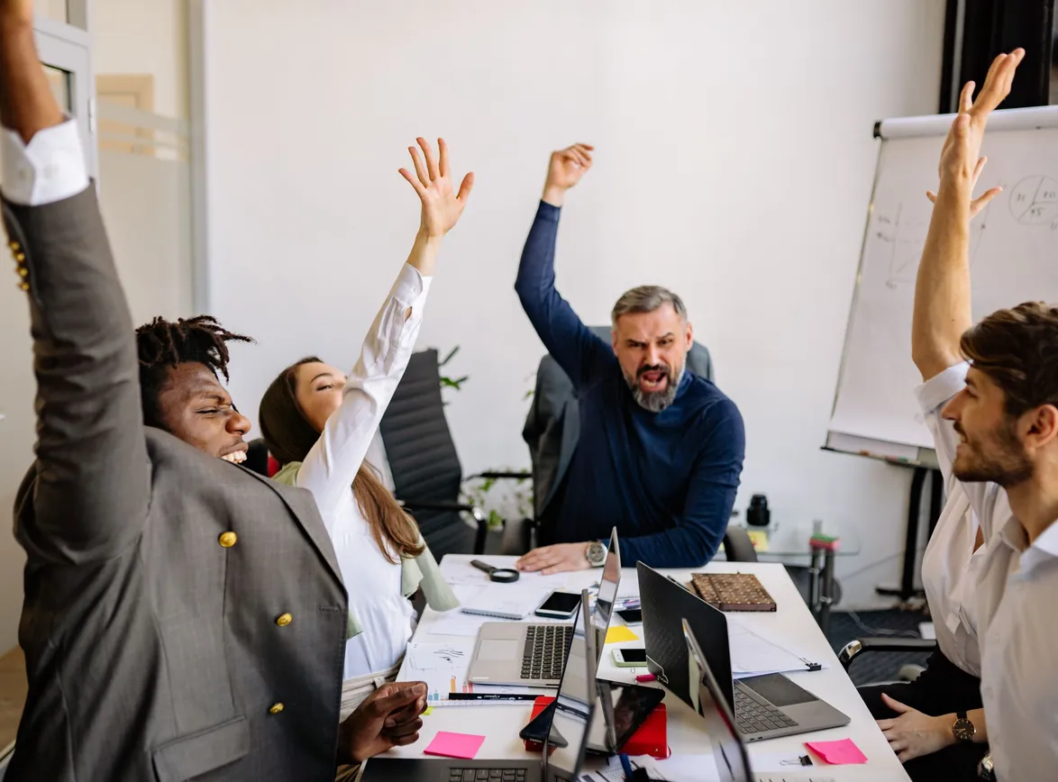 Business team raising hands in excitement during a meeting in a modern office