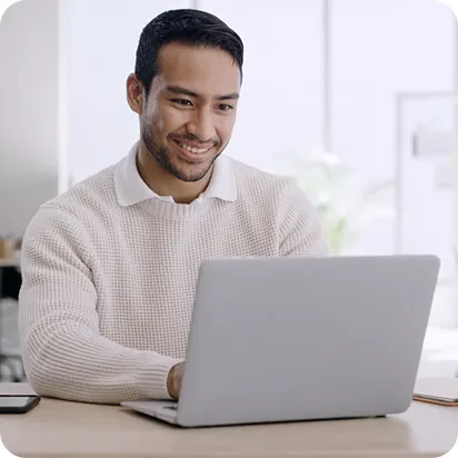Sales rep in a knit sweater smiling while working on a laptop at a desk