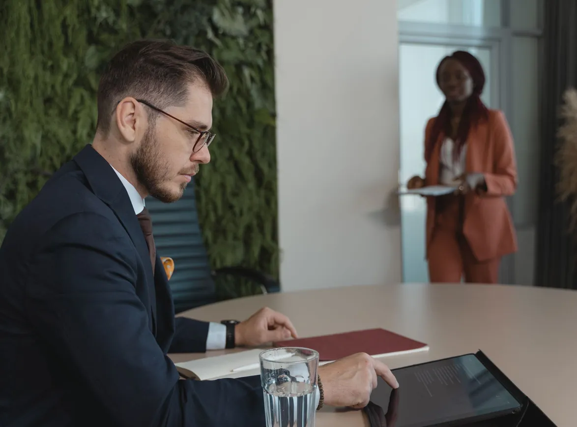 Focused businessman using tablet in modern office with green wall and colleague in background