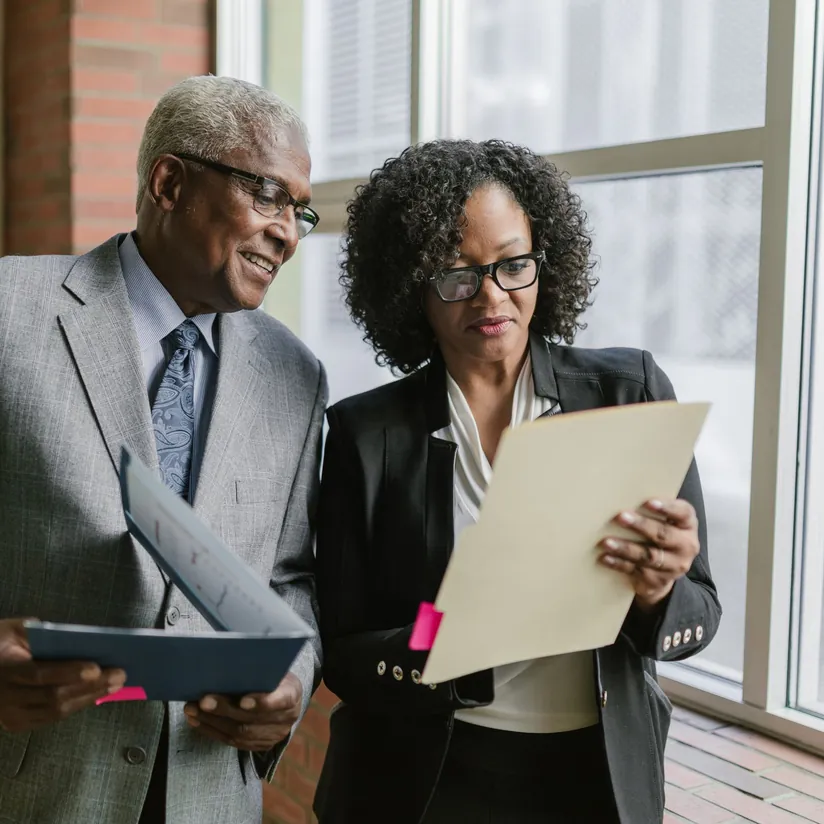 Two executives reviewing documents in folders beside an office window