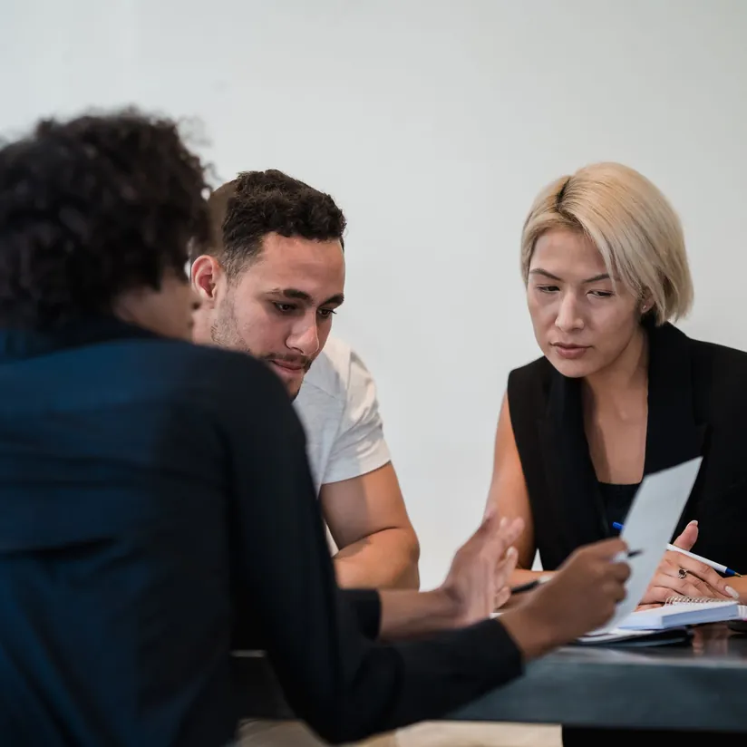 Three colleagues at a table reviewing a sheet of paper together, one holding a pen over a notebook