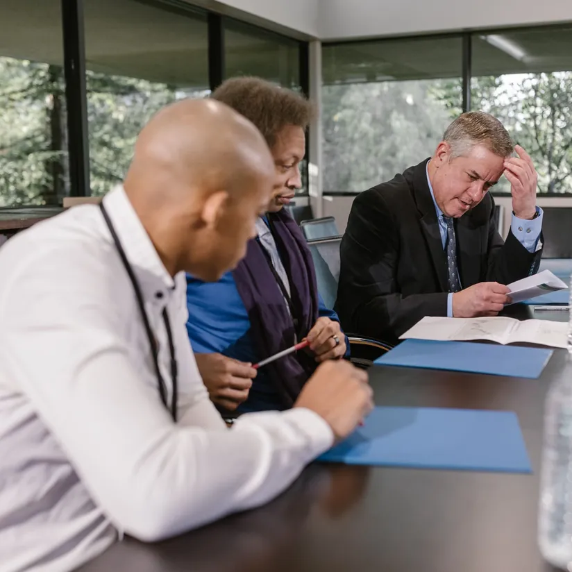 Worried executive holding his forehead while reviewing documents with two colleagues at a conference table