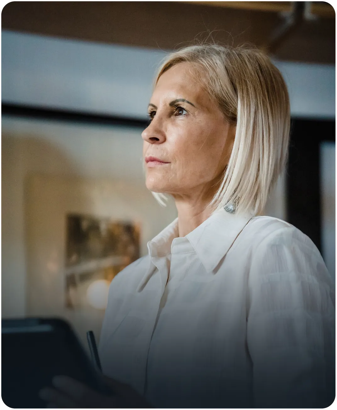 Businesswoman in a white shirt holding a tablet and stylus while looking ahead in an office