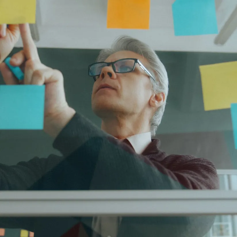 Man in glasses arranging blank colored sticky notes on a glass planning board
