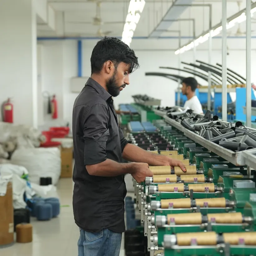 Worker checking thread bobbins on a winding machine along a bright factory production line