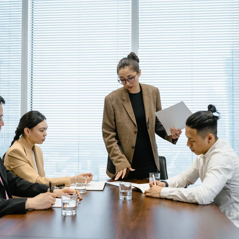 Consultant standing at a boardroom table walking colleagues through printed documents