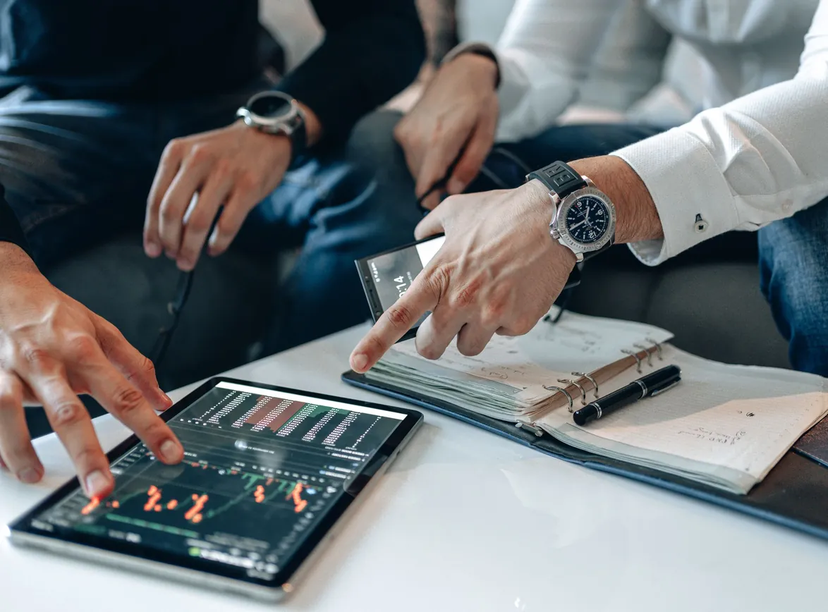 Men in business attire discussing financial data on a tablet indoors