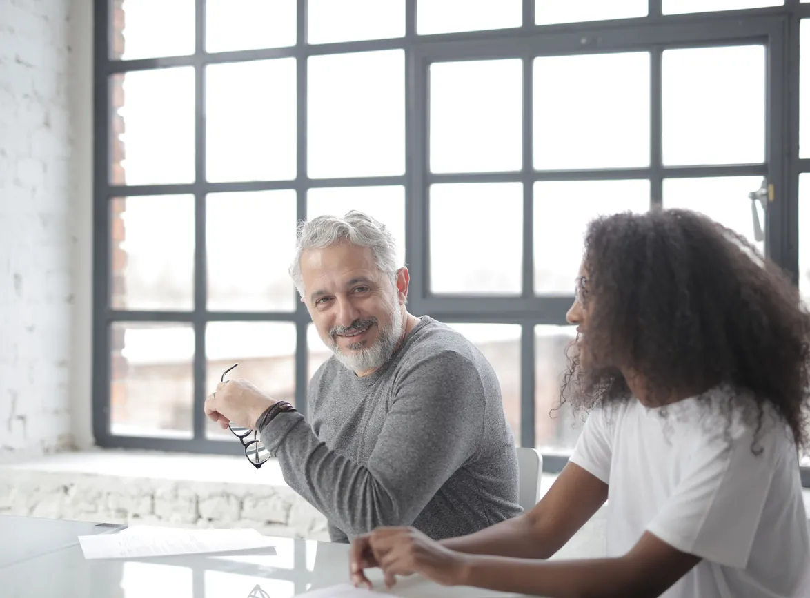 Happy aged gray haired coach in casual wear looking at camera while supporting young Black coworker