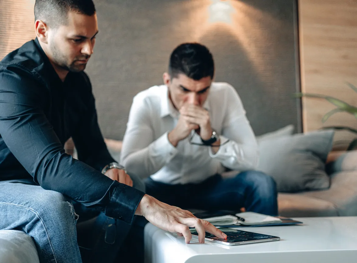 Two men engaged in a serious discussion, analyzing data on a tablet indoors