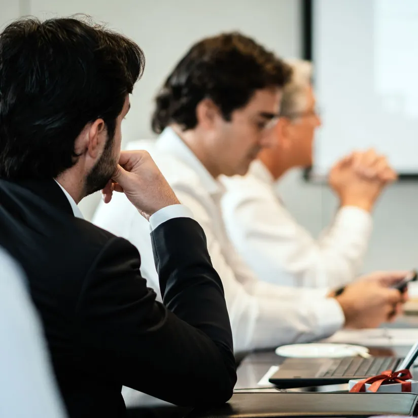 Businessman resting his chin on his hand during a meeting as colleagues work on a laptop and phone
