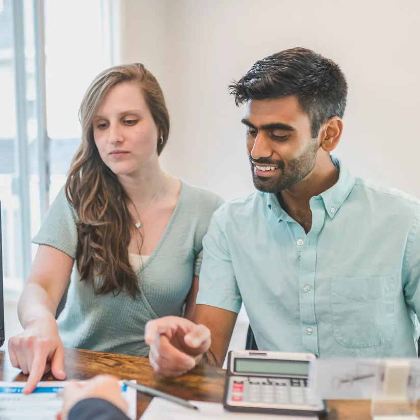 Young couple meeting a financial advisor at a desk with a calculator and paperwork