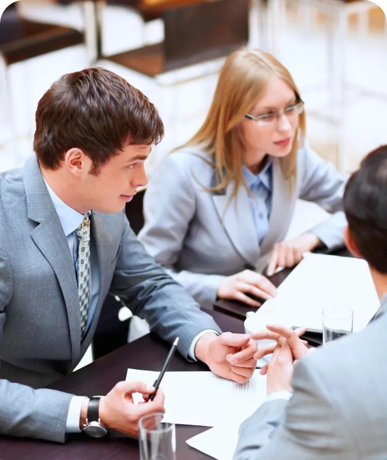 Three business professionals talking across a table with documents and glasses of water