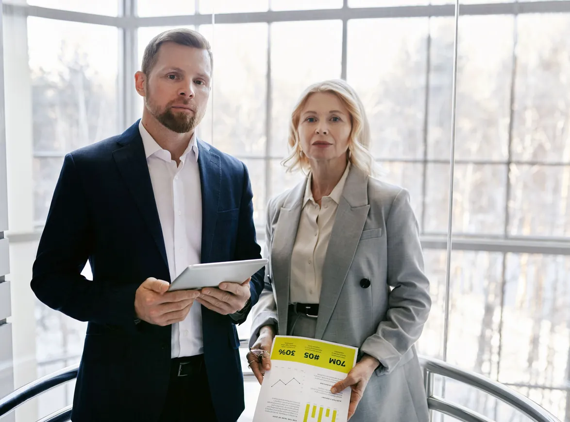 Two business professionals in a modern office discussing a project with a tablet and report