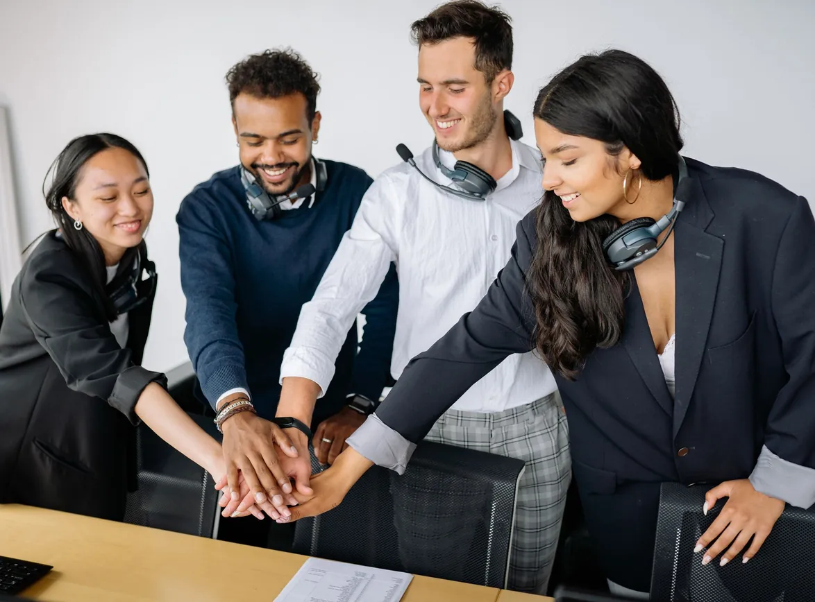 A group of call center agents in an office joining hands in a teamwork gesture, smiling and wearing headsets