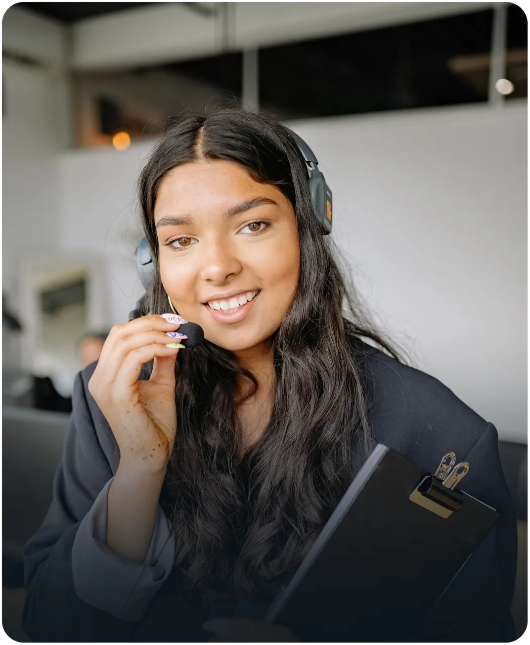 Smiling customer support agent adjusting her headset microphone while holding a clipboard in an office