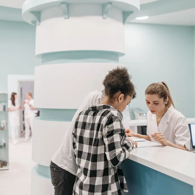 Patient reviewing paperwork with a receptionist at a clinic front desk