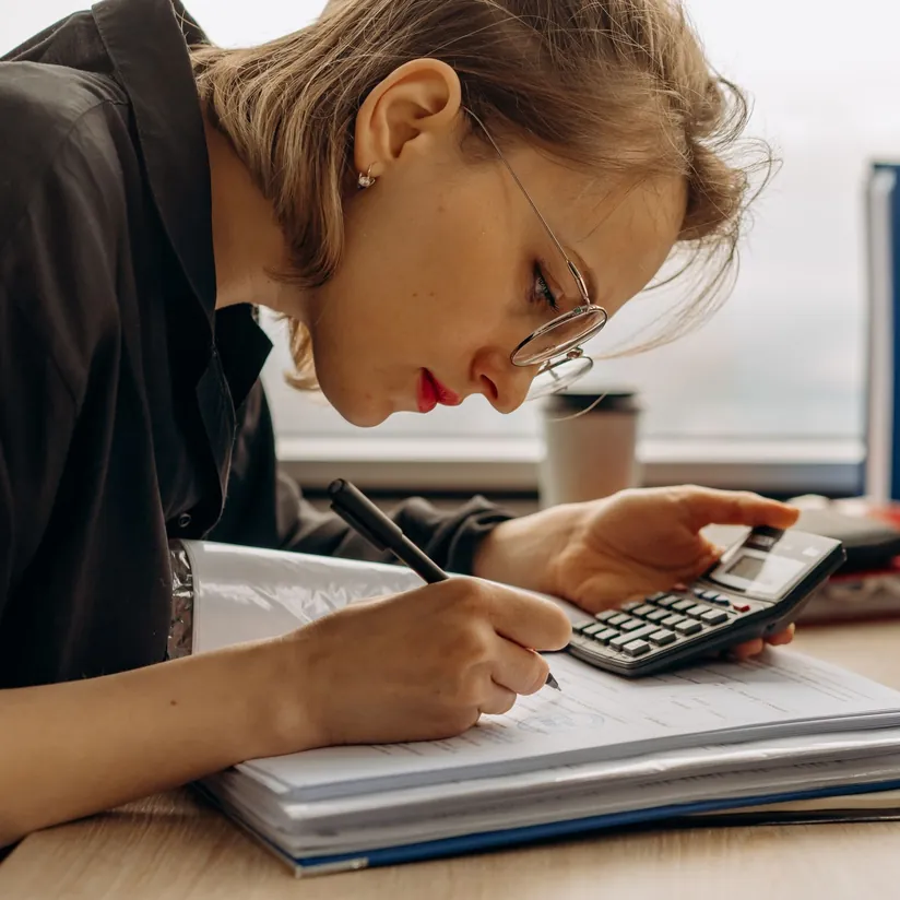 Accountant writing in a thick binder of paperwork while using a calculator