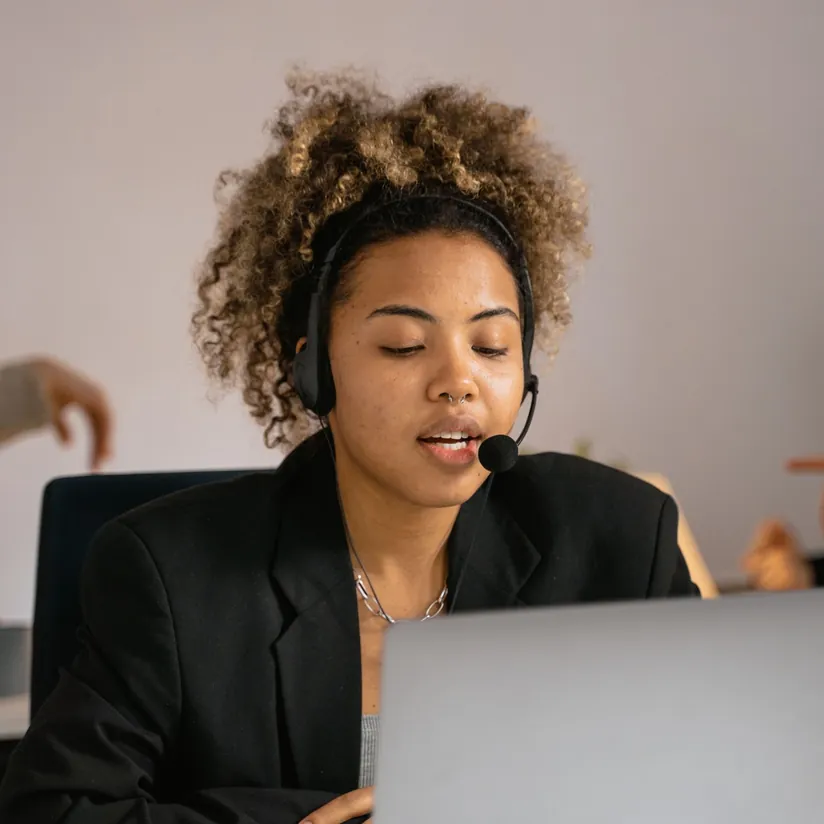 Customer support agent wearing a headset speaking into the microphone while working on a laptop