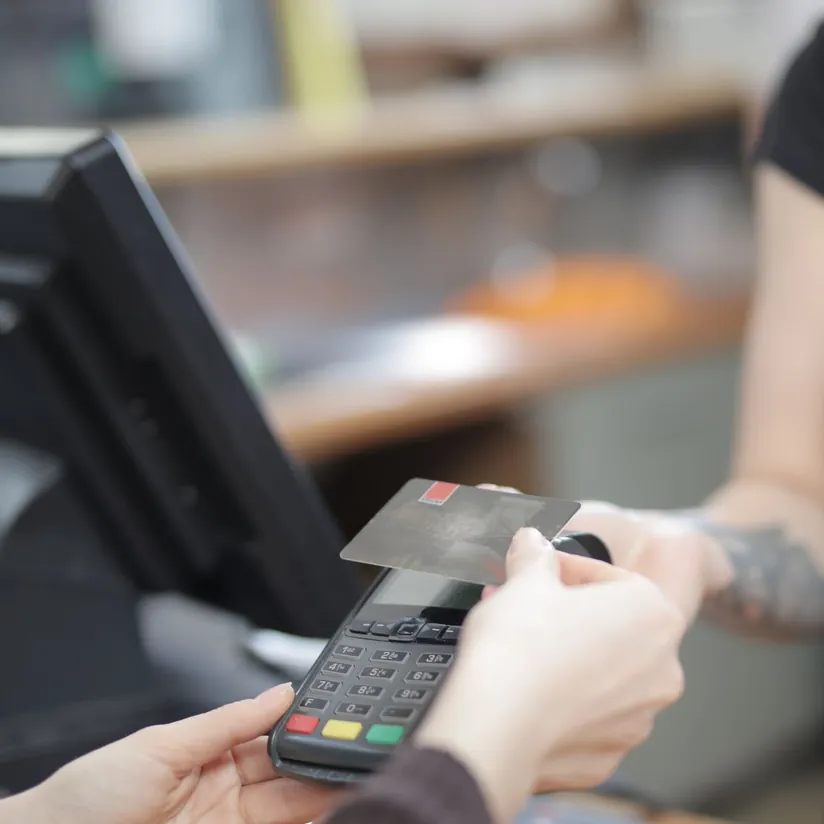 Customer tapping a payment card on a handheld card terminal at a store checkout counter