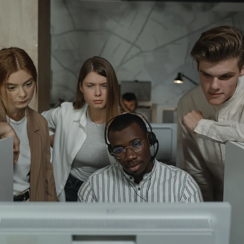Analyst wearing a headset at a monitor as three colleagues lean in to watch his screen