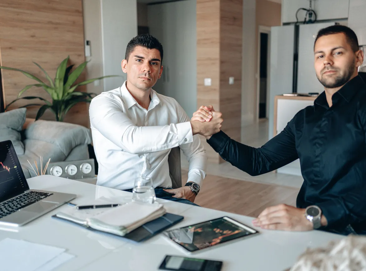 Two professionals agreeing on a deal while sitting at a desk in an office setting