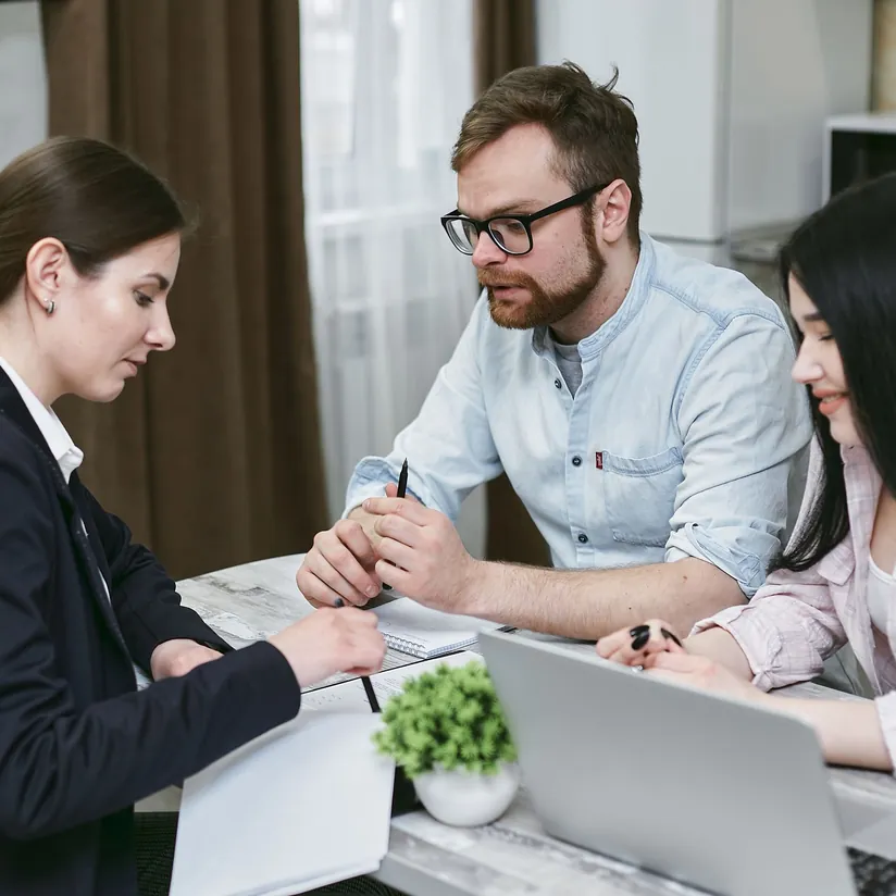 Loan officer reviewing paperwork with a couple across a table with a laptop and notebook