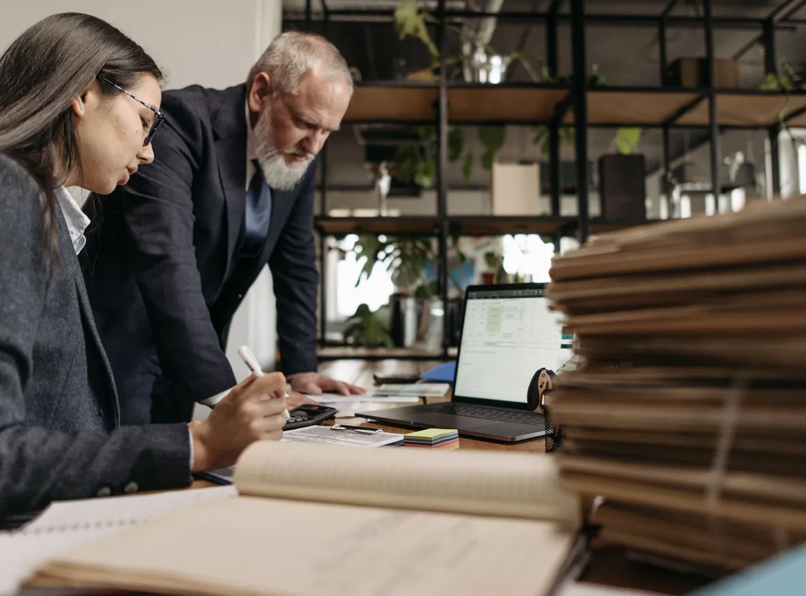 Two colleagues in business attire working together at a desk in a modern office
