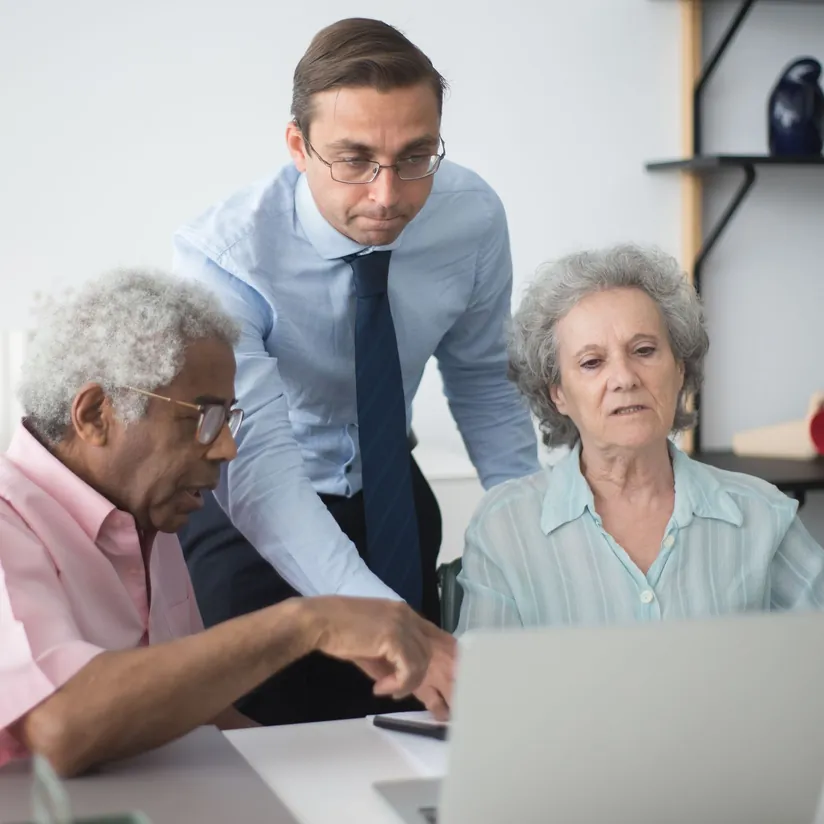 Financial advisor standing behind an older couple as they review a laptop screen together