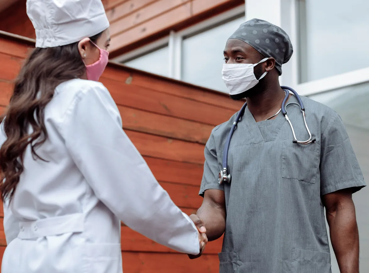 Two healthcare workers in face masks shaking hands outdoors