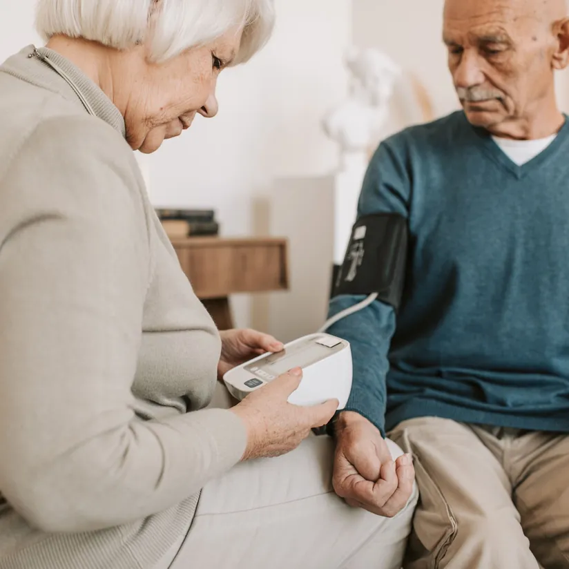 Senior woman holding a home blood pressure monitor while measuring her husband's blood pressure