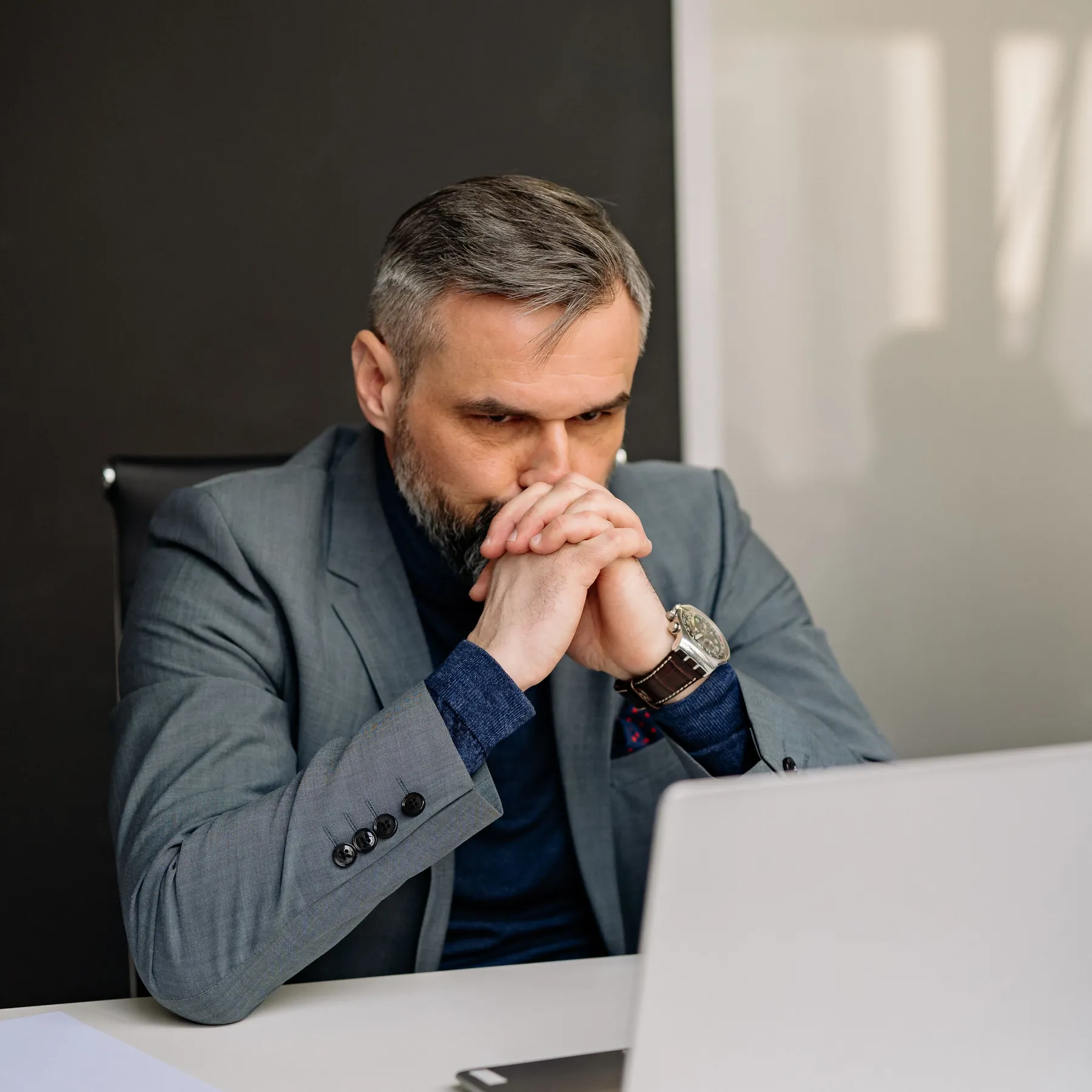 Senior executive with clasped hands staring at a laptop, weighing a stalled AI pilot