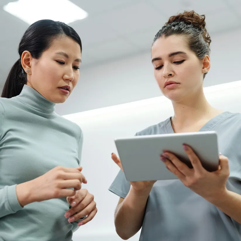 Clinician in gray scrubs reviewing information on a tablet with a woman in a bright clinic