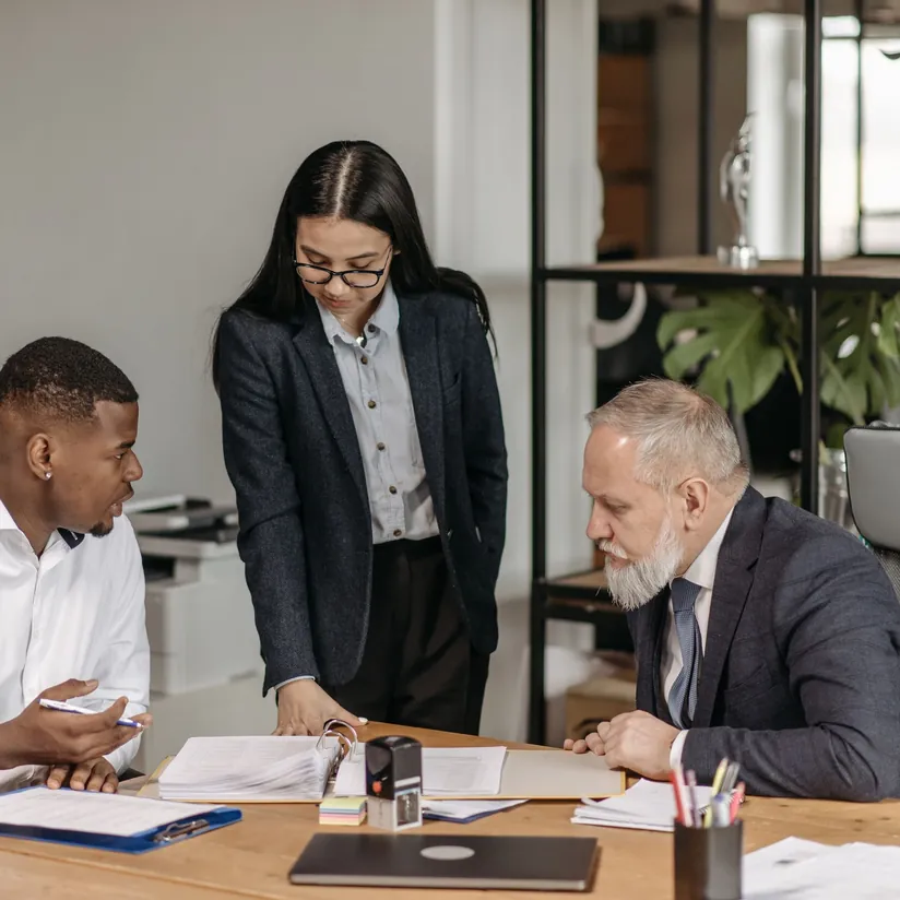 Three professionals reviewing a binder of documents at an office table with a stamp and folders