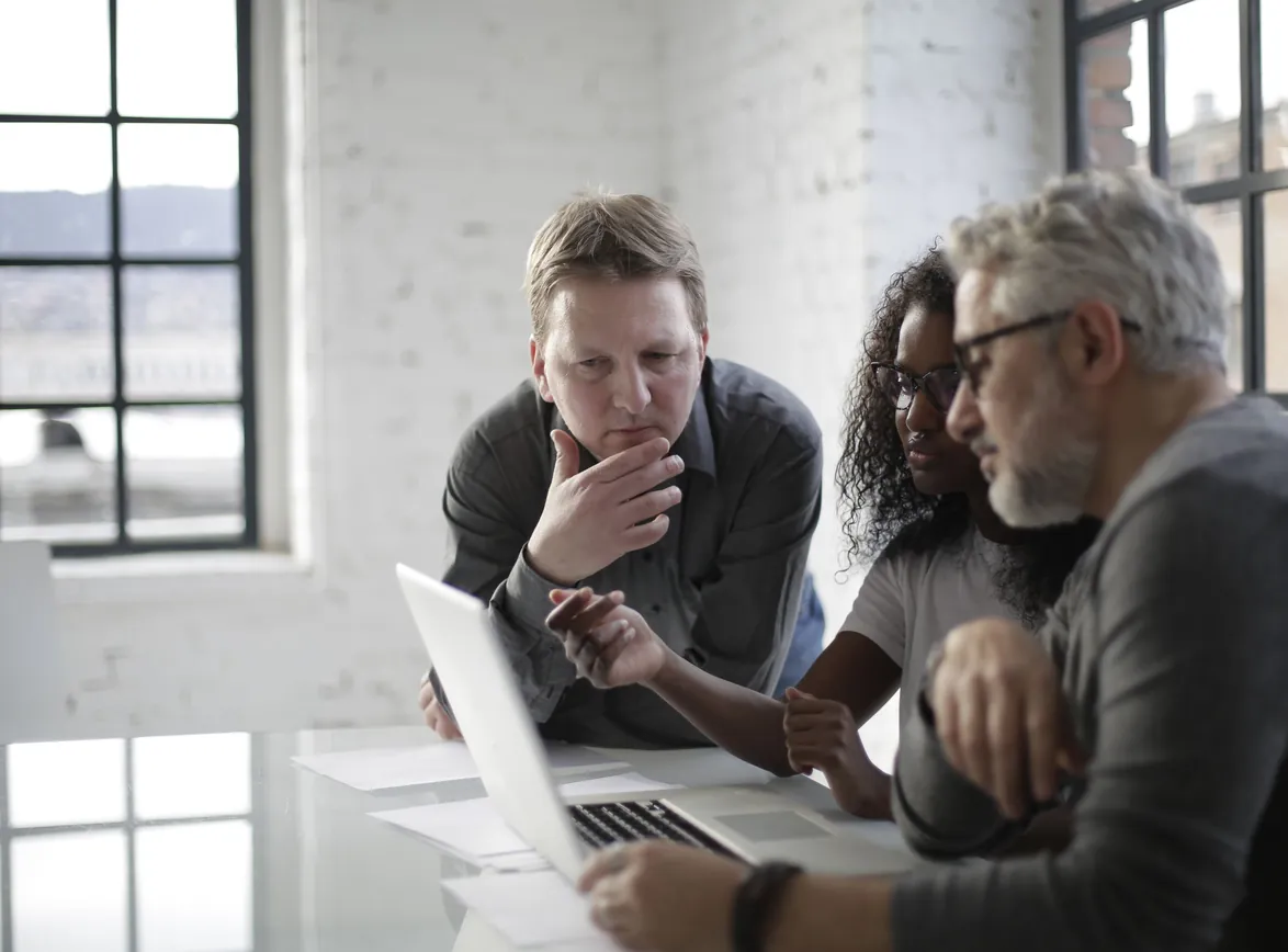 Concentrated serious multiracial people discussing details of creative project while sitting at table and using laptop