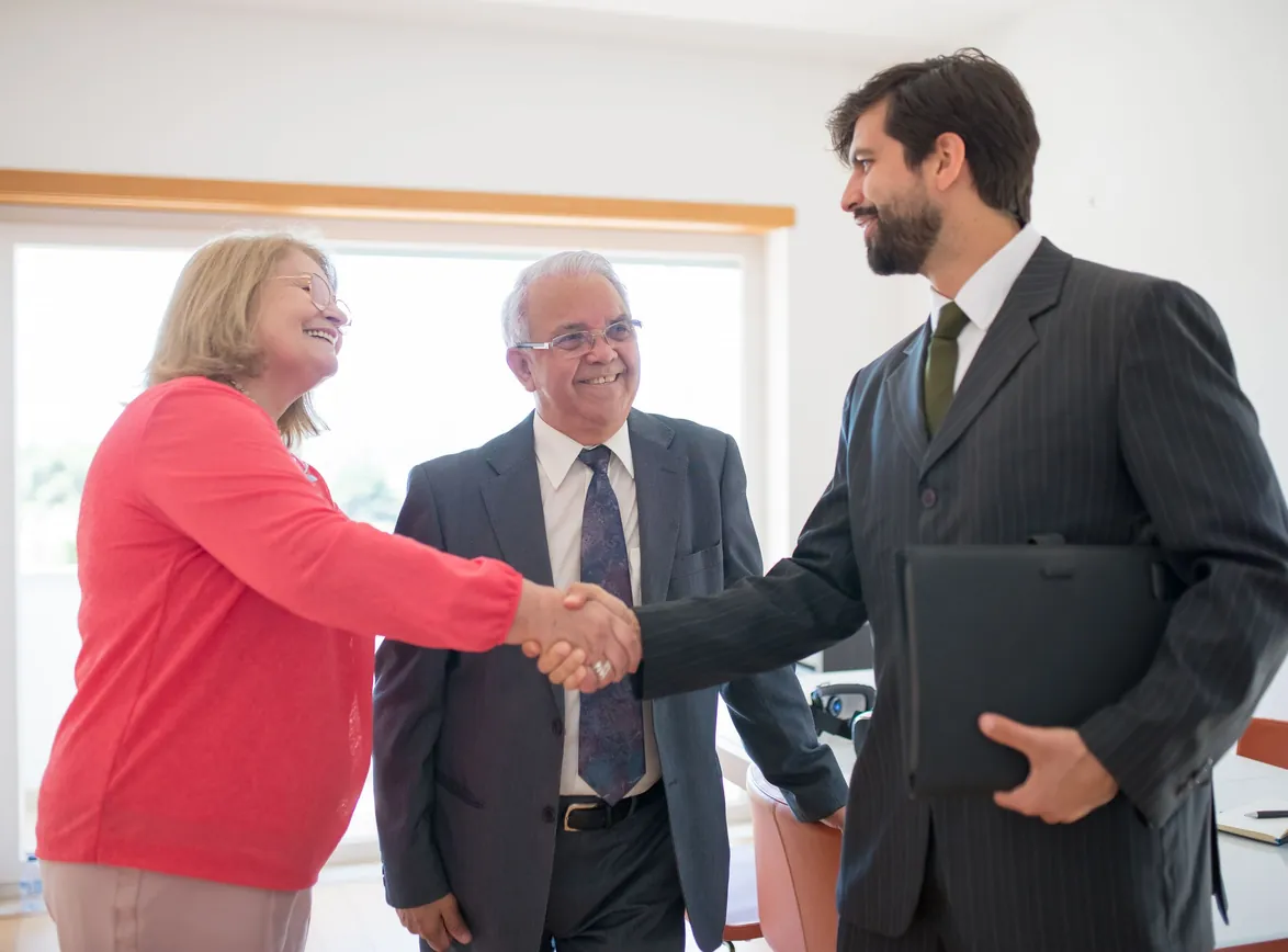 Two older clients shaking hands with an advisor indoors