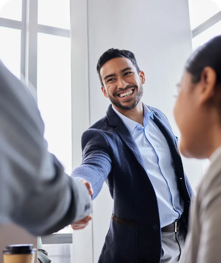 Smiling businessman in a navy blazer shaking hands with a colleague in a bright office
